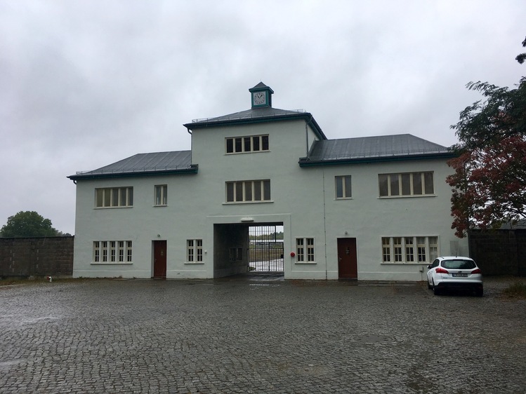 An off-white building with a gate in the middle, set against a grey sky.